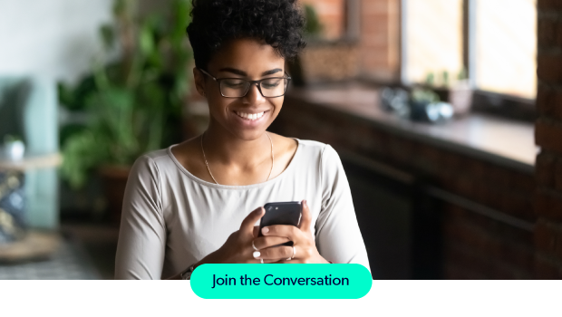 A smiling woman with glasses looking at her smartphone in a cozy kitchen.